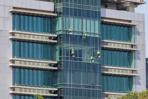 Window cleaners work as a team to clean the glass front of a hospital in downtown Bangkok, Thailand