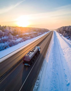 Petrol cargo truck lorry tanker driving on highway hauling oil products at sunrise, wide snowy