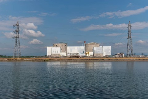 A large industrial nuclear power plant is located on a quiet water front. Two tall cylindrical