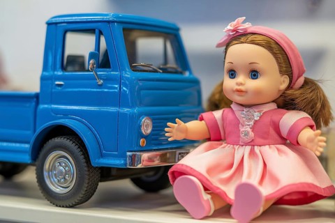 Cute doll in pink dress and blue toy car. Gender stereotypes in children's toys and color coding