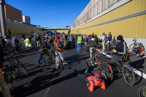 Cyclists wait to continue their journey. Meanwhile, a woman wearing a helmet is lying on the