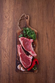 Freshly sliced lamb chops, with herbs and vegetables, on a wooden board, ready to cook, on a wooden