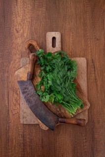 Fresh cilantro and dill are placed on a wooden cutting board next to a machete. The herbs are