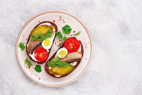 Sandwiches on rye bread, with sprats, quail eggs, fresh tomatoes and pickled cucumber, appetizer,