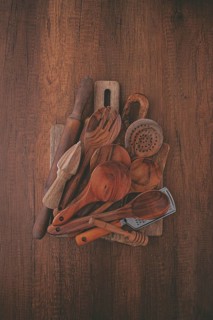 A variety of wooden kitchen utensils are arranged on a dark brown wooden surface. Items include