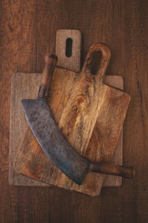 A large curved knife rests on top of two wooden cutting boards on a rustic surface. The knife shows