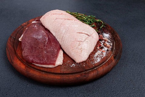 Fresh raw duck breasts, on a wooden chopping board, with herbs and spices, no people