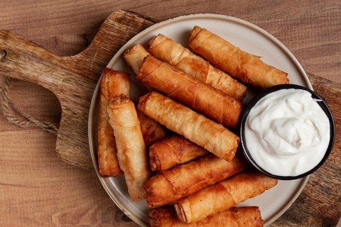 Fried spring rolls with cheese, on a wooden background, with cream sauce, no people