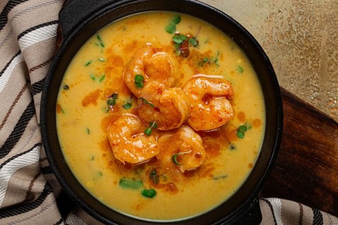 Creamy shrimp curry with spices, garnished with herbs, on a textured background, homemade, no