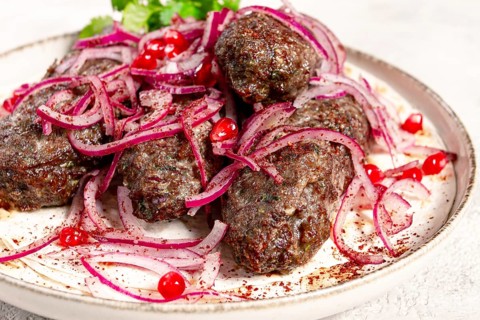 Grilled kebabs topped with onions and pomegranate on a white plate in a bright kitchen setting