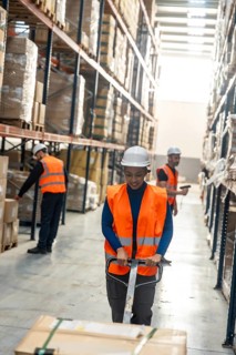 Diverse logistics team preparing packages and moving products on pallet jacks inside a modern
