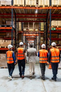 Diverse team of manager and warehouse workers in safety vests and hard hats walking through a