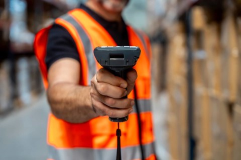 Warehouse worker wearing a safety vest using a barcode scanner to manage inventory and streamline