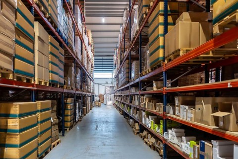 Storage warehouse interior filled with numerous cardboard boxes and products stacked on tall racks,