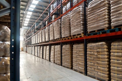 Spacious industrial warehouse aisle with pallets of identical sacks stacked on tall metal shelving,