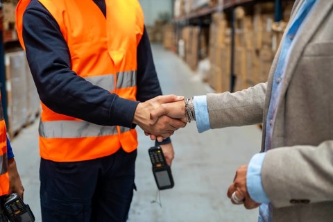 Two people, one wearing a safety vest and scanner, the other in a business suit, shaking hands in a