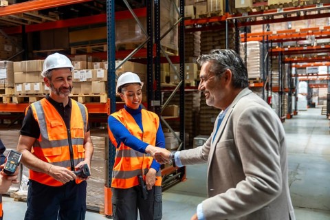 Manager shaking hands with a woman warehouse worker while male team members smile, symbolizing