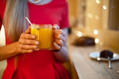A woman in a bright red dress holds a glass of warm orange drink, enjoying a relaxing moment. Soft