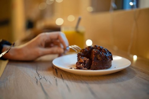 A hand reaches for a fork to savor a piece of rich chocolate dessert on a plate. Soft lighting