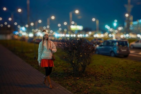 A woman walks along a city street at night, wearing a warm outfit that includes a short coat,
