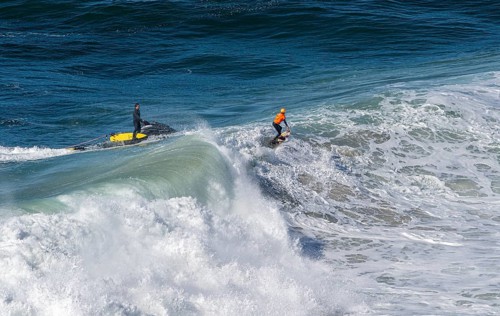 Surfers with their jet ski pilots in the Atlantic waves below Farol de Nazaré, Forte São Miguel,