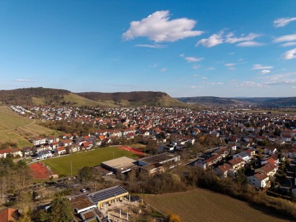 Large-scale city view with sports field in the foreground, surrounded by hills and blue skies, Korb