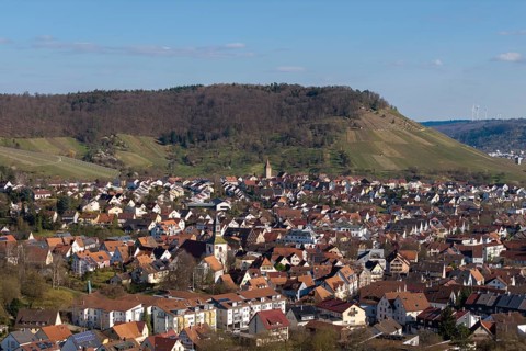 City view with hills in the background, lots of red house roofs and green surroundings under blue
