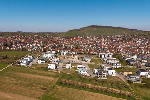 View of city with new development area, red roofs and surrounding green hills in the background,