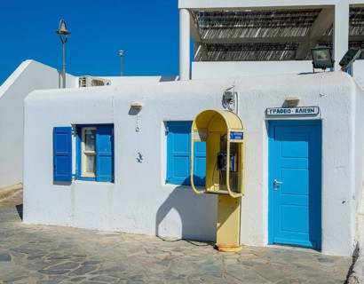 Mykonos, Cyclades, Greece - Old yellow telephone box in front of white house with blue shutters in