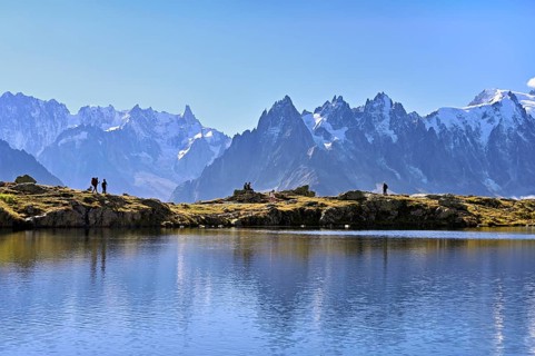 A group of hikers at Lac de Chésserys, behind the snow-covered Mont Blanc massif,