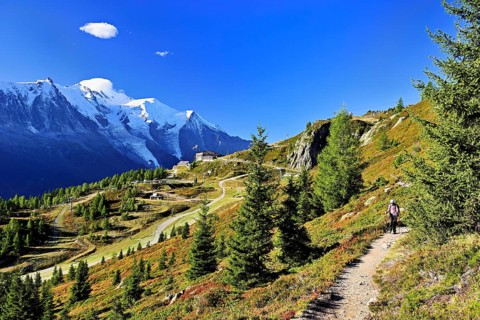 Female hiker on a hiking trail with the La Flégère cable car mountain station and the snow-covered