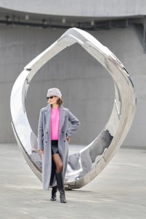A woman stands confidently in urban attire against a shiny modern sculpture. The scene showcases