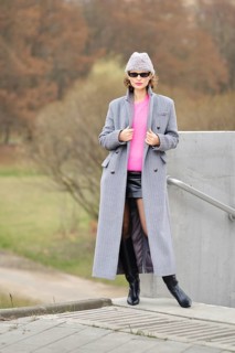 A woman showcases striking urban fashion by wearing a bright pink sweater, a long gray coat, and