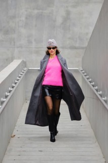 Model walks confidently in urban fashion featuring bright pink sweater and stylish coat