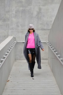 A stylish woman walks down a sleek urban walkway, dressed in a stylish gray coat over a bright pink