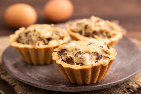 Tartlets with meat and cheese on brown wooden background and linen textile. side view, close up,