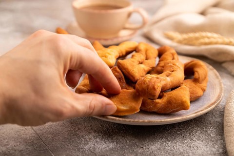 Crunchy biscuit Brushwood cookies with hand sprinkled with powdered sugar on brown concrete