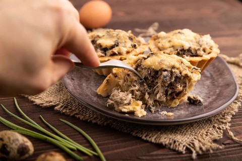 Tartlets with meat and cheese with hand on brown wooden background and linen textile. side view,
