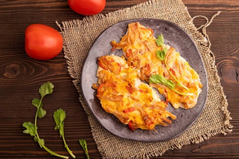 Baked chicken meat with cheese and tomatoes on brown wooden background and linen textile. top view,