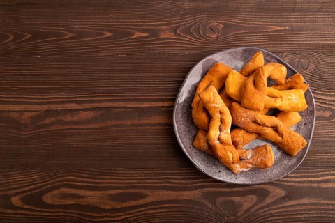 Crunchy biscuit Brushwood cookies sprinkled with powdered sugar on brown wooden background, top