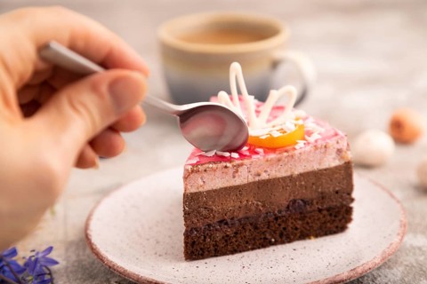 Chocolate cake with hand on brown concrete background, cup of coffee, side view, close up,