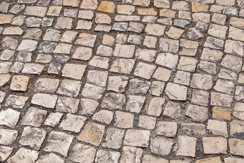 Irregular paving stones in shades of beige and gray create an antique street texture, Portugal