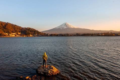 Young man standing on rocks in Lake Kawaguchi, view of Mount Fuji volcano at sunset, Yamanashi
