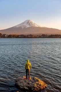 Young man standing on rocks in Lake Kawaguchi, view of Mount Fuji volcano at sunset, Yamanashi