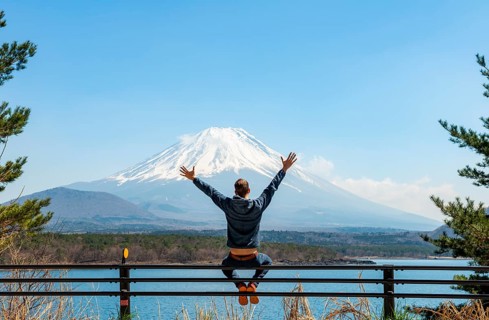 Young man sitting on railings next to a road and stretching his arms in the air, looking across the