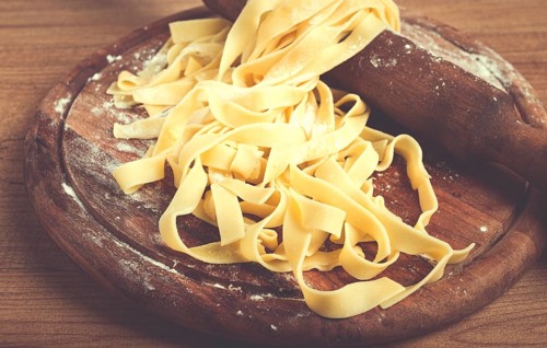 Raw tagliatelle pasta, homemade, on a rolling pin, top view, on a cutting board, cooking concept