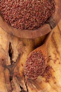 Natural, red rice, in a wooden bowl and spoon on a wooden surface in rustic style, top view