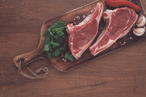 Freshly sliced lamb chops, with herbs and vegetables, on a wooden board, ready to cook, on a wooden