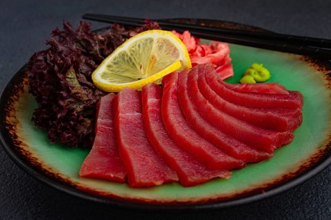 Fresh tuna sashimi served with lemon, wasabi, and pickled ginger on a dark background