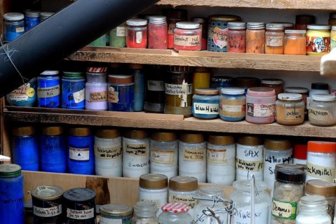 Glasses with various color powders and pigments on a wooden shelf, artist workshop, Zurich,